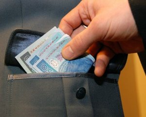 Dłoń trzymająca plik banknotów, próbująca włożyć je do kieszeni policyjnego munduru