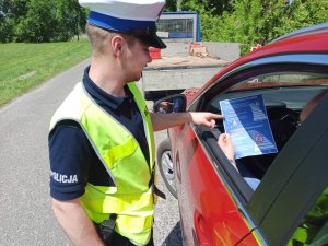 Policjant ruchu drogowego, pokazujący kierującemu najważniejsze zmiany w przepisach ruchu drogowego na przekazanej broszurze informacyjnej.