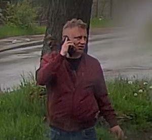 Mężczyzna trzymający telefon w prawej ręce w bordowej kurtce.