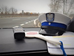 Na zdjęciu na podszybiu radiowozu znajduje się czapka policyjna, tarcza do zatrzymywania pojazdów oraz stacja do kontaktowania się pomiędzy policjantami.