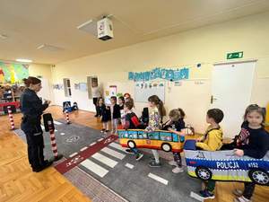 Zdjęcie, na którym policjantka pokazuje grupie dzieci naukę przepisów przez mobilne miasteczko ruchu drogowego.