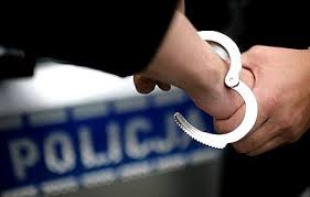 Grafika przedstawiająca zakładanie kajdanek na rękę, w tle napis POLICJA